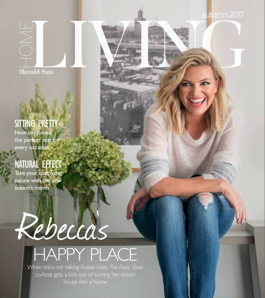 A photo of the Home Living magazine cover, where Rebecca Maddern is sitting at home in blue jeans and a light knit jumper, surrounded by fresh flowers.