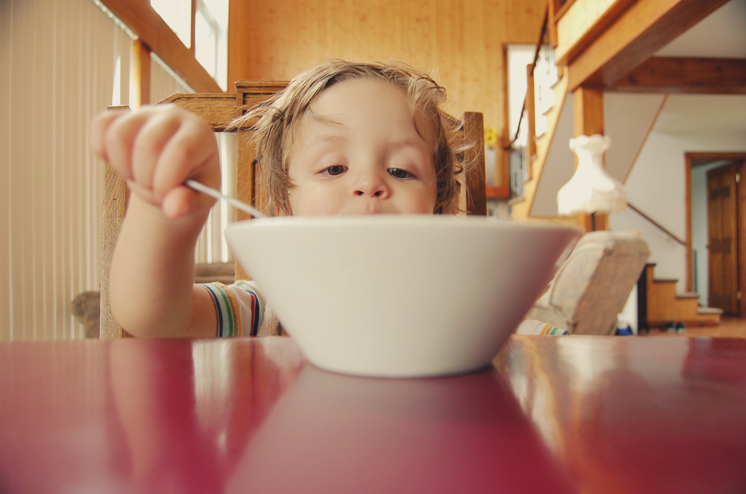 A child is holding a spoon and peering excitedly into a bowl