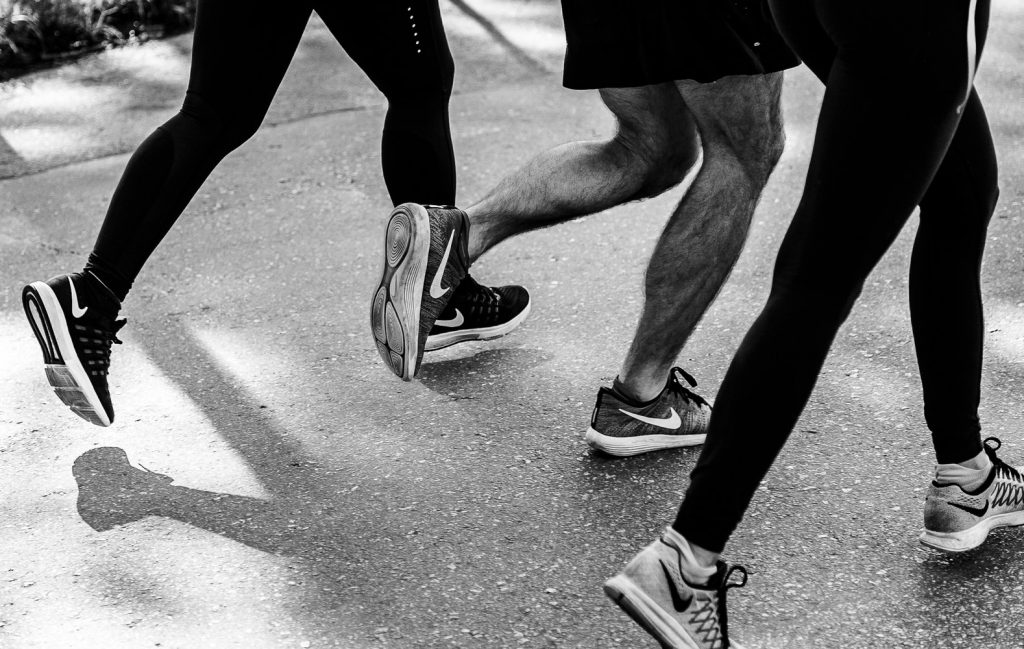 Three men are jogging on the footpath in sneakers