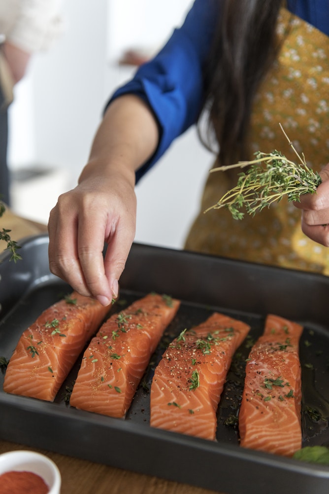 A woman in an apron prepares salmon fillets on a tray