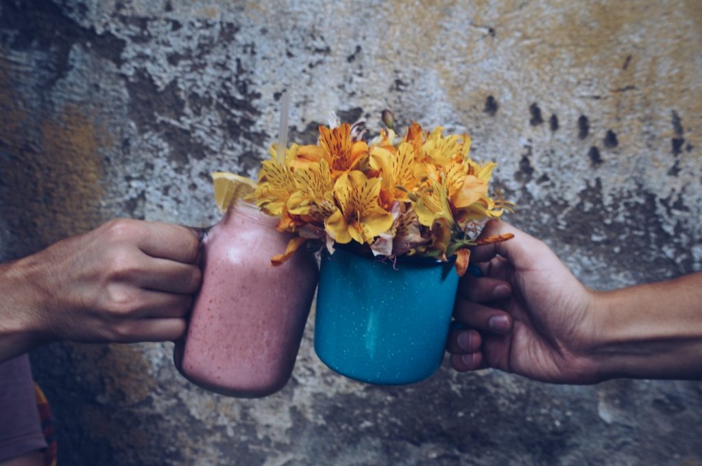 Two hands each holding a colourful smoothie with flowers on top