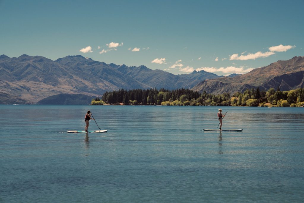 Two women paddleboarding with mountains in the background