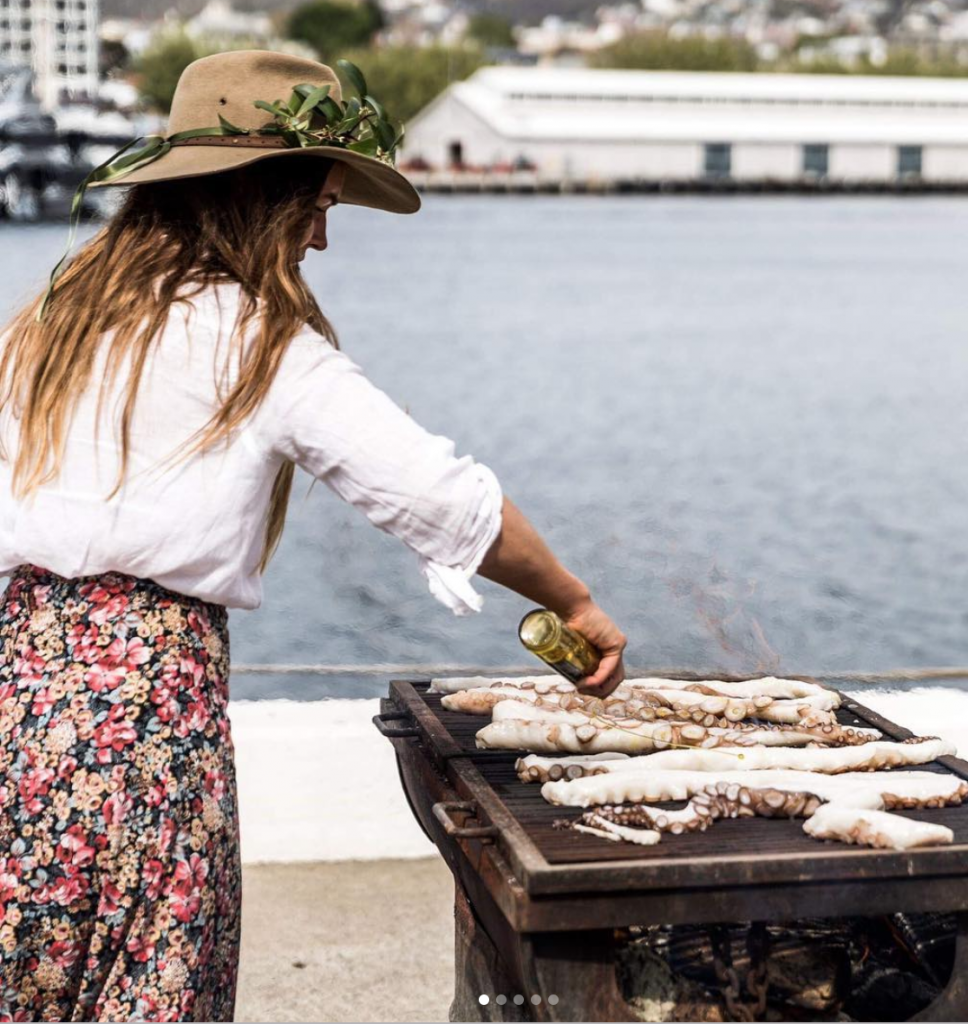 A woman in a hat cooks a seafood barbecue by the water