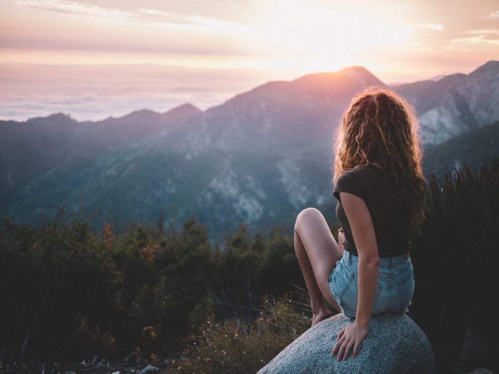 A woman sits solo on a mountain watching the sunset