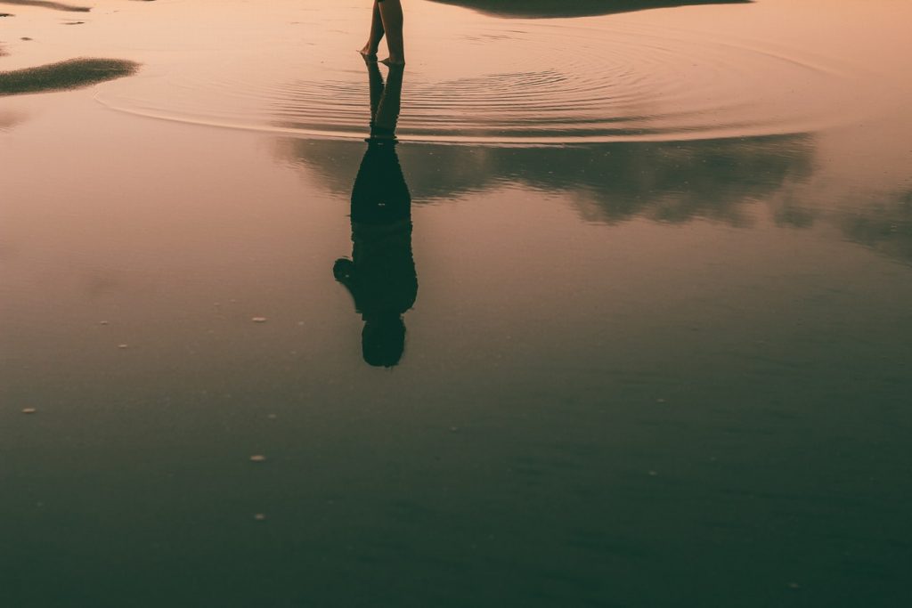 A woman's silhouette is reflected in the water at sunset 
