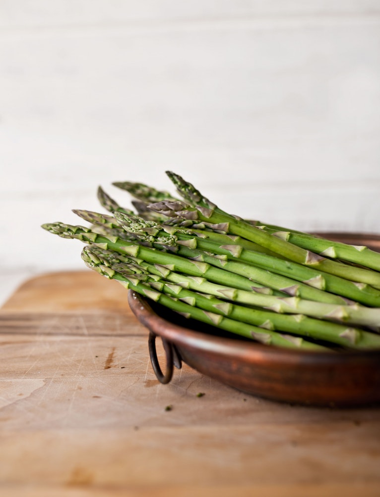 A bunch of asparagus in a bowl on a bench