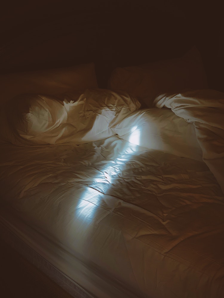 A stream of light shines on an unmade bed