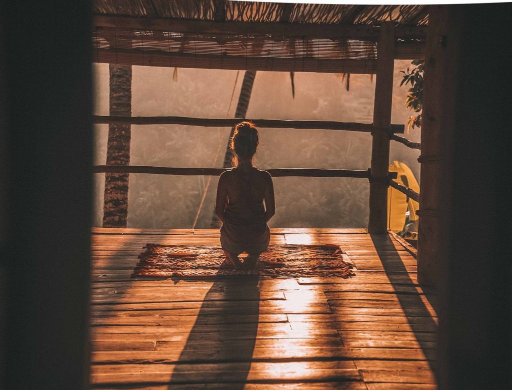 A woman meditating on a timber deck in the jungle