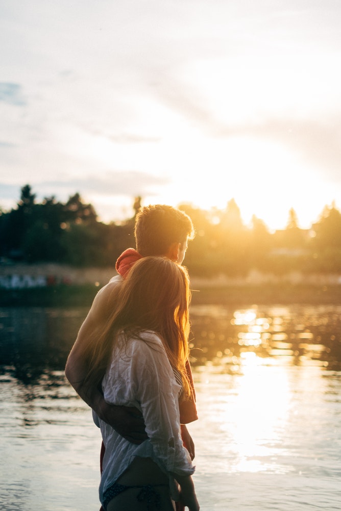 A couple embraces while walking along a riverbank at sunset