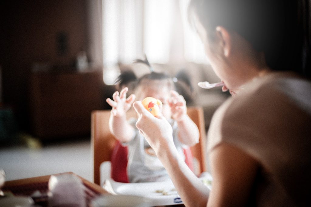 A mother feeds her daughter in her high chair