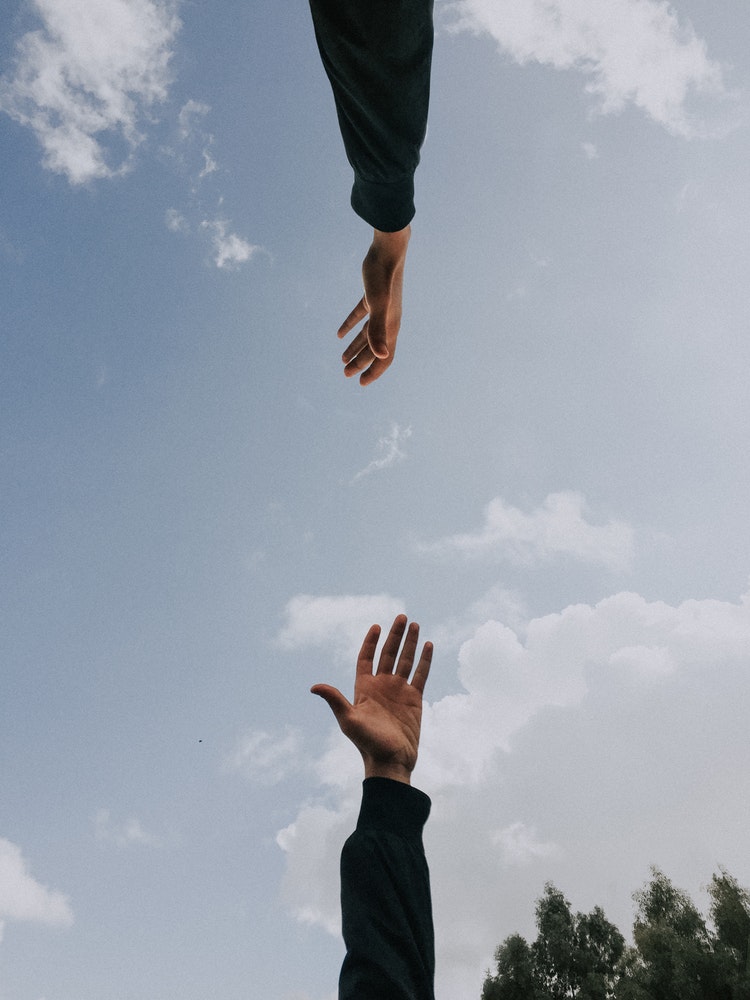 Two hands reach for each other under the blue sky