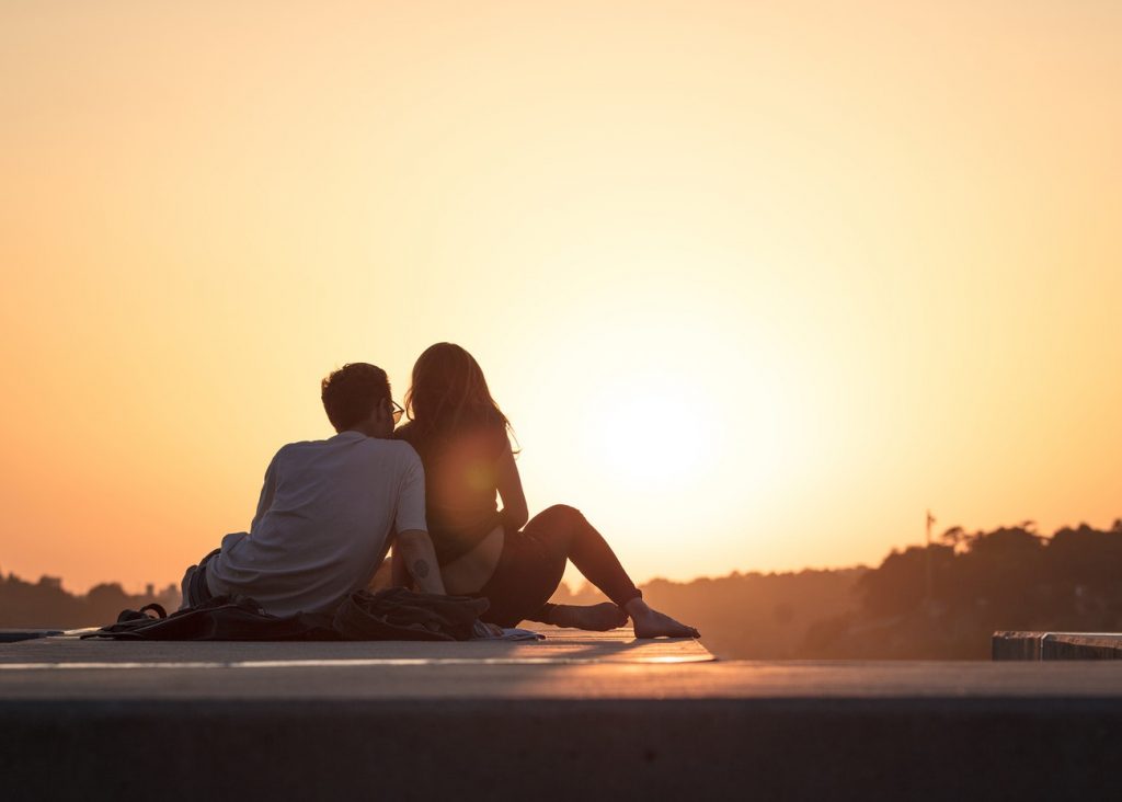 A couple leans against each other on a rooftop while watching the sunset