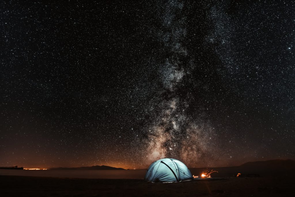 A night-time shot of a tent pitched in the middle of a field, surrounded by stars