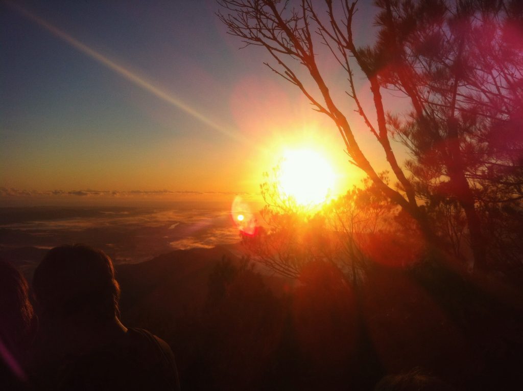 Friends watch the sun rise from Mount Warning