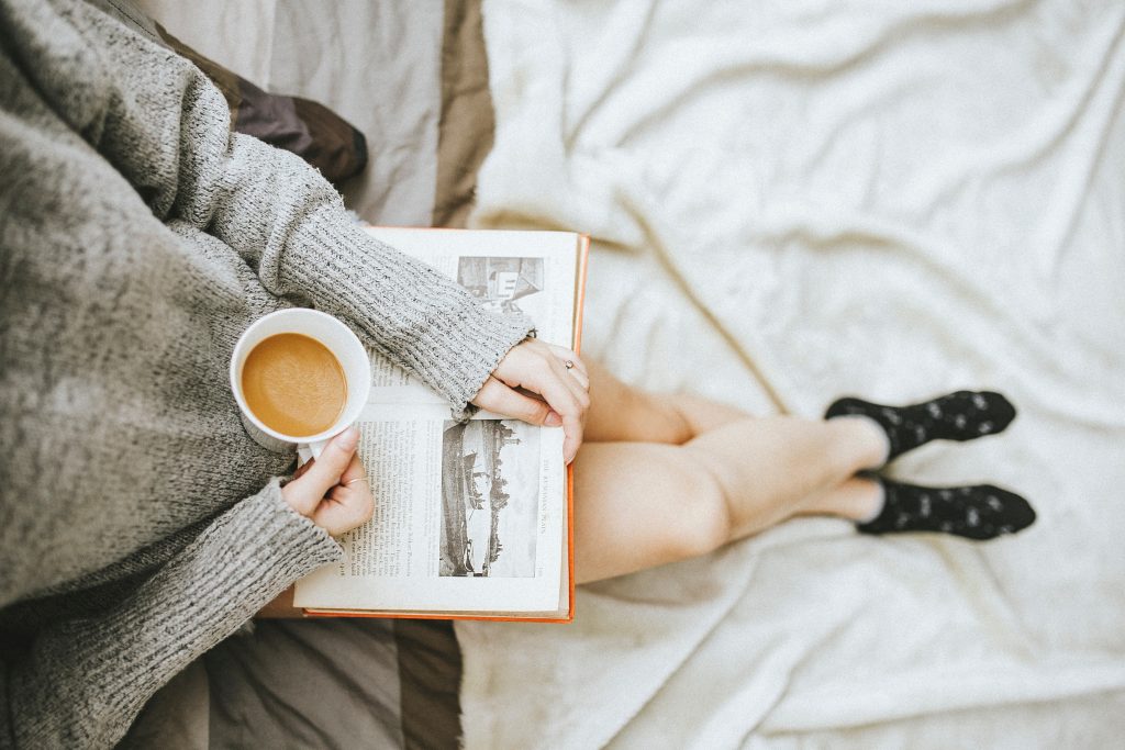 A woman reads a book while sitting and drinking a cup of coffee