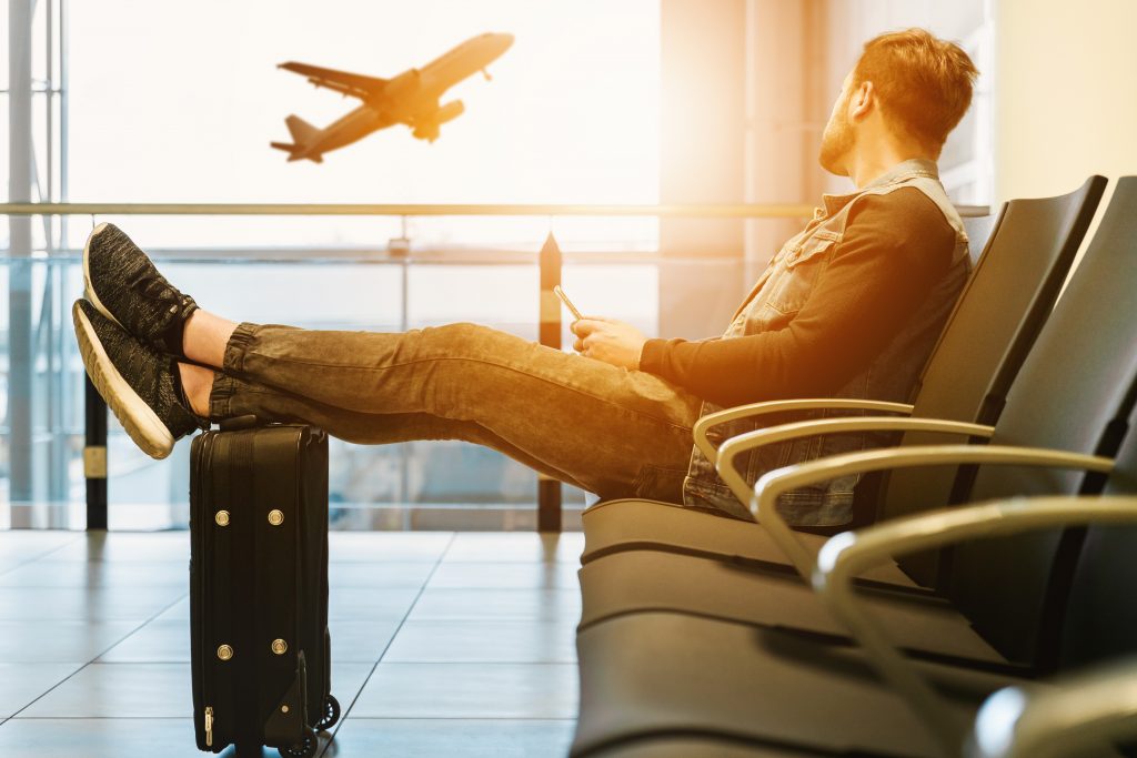 A man sits on a chair in an airport, watching the planes taking off
