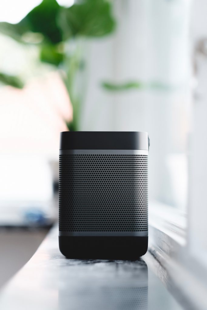 A black portable speaker sits on a bench in a bedroom