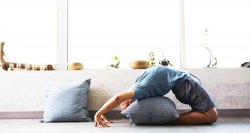 A man practices a yoga backbend over a cushion in his minimalistic zen zone