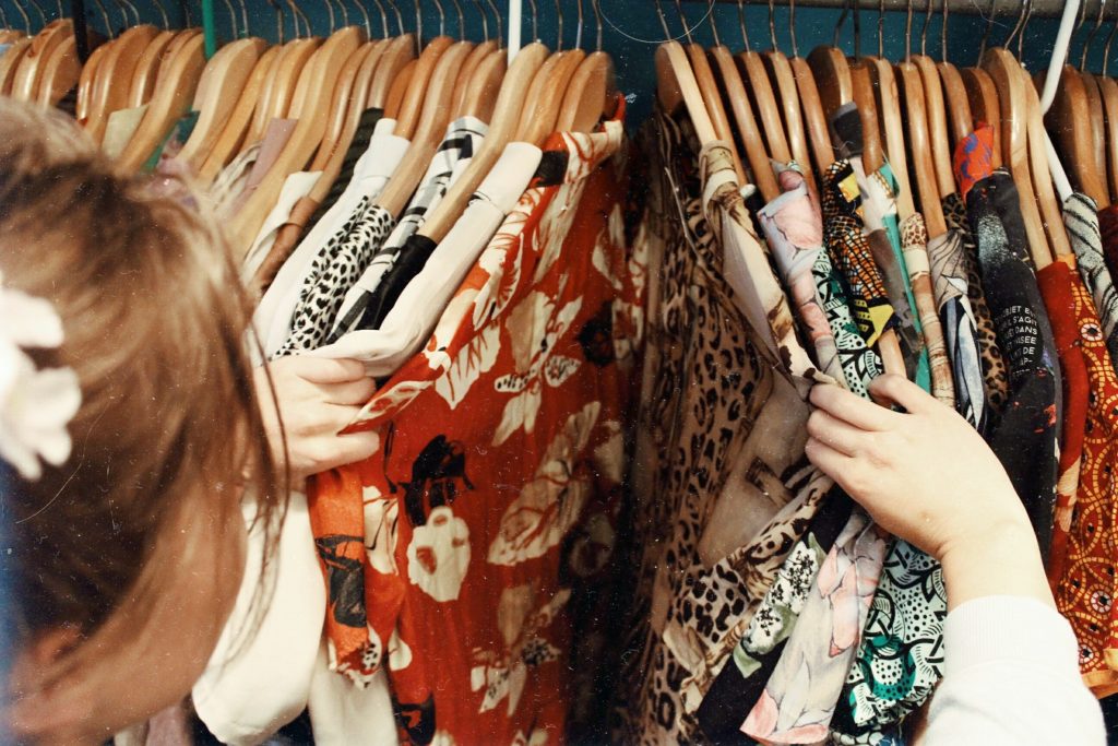 A woman searches through various colourful shirts on a clothing rack