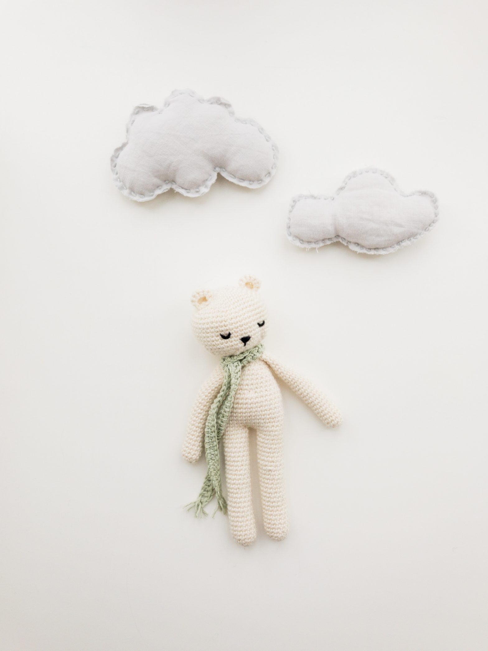 A woollen soft toy is flat-layed with two toy clouds
