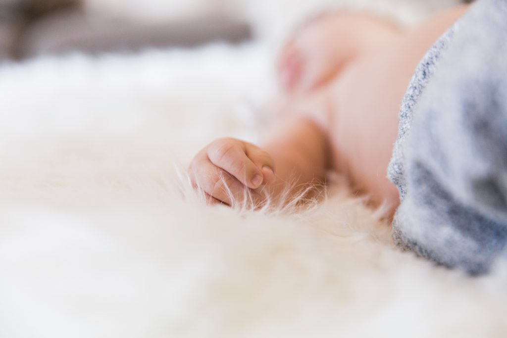 A baby in a blue beanie lays on a white rug